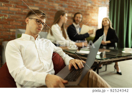 Portrait of concentrated young man, manager working on laptop at stylish office. 92524342