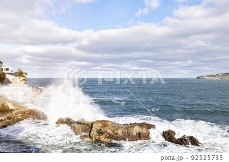 Waves breaking on rocks on the shore overlooking a coastal town. Concept vacation Waves breaking on rocks on the shore overlooking a coastal town. Concept vacation 92525735