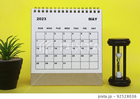 May 2023 desk calendar with table plant and minutes glass on yellow background. 92528036