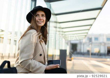 Stylish woman with smartphone in hand sits at a public transport stop Stylish woman with smartphone in hand sits at a public transport stop 92529021