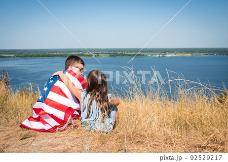 Happy kids with the flag of america are sitting in a field on the background of the bay 92529217