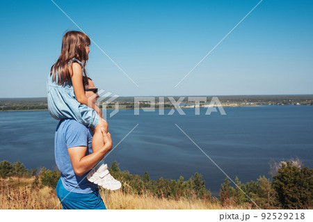 Happy father with his daughter having fun and playing in nature. The child sits on the shoulders of his father. Side view 92529218