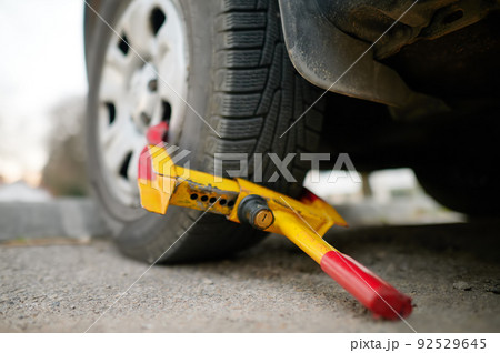 Car wheel blocked by wheel lock. Illegal parking of automobile. Wheel of automobile was locked with clamped tire boot. Parking violations. 92529645