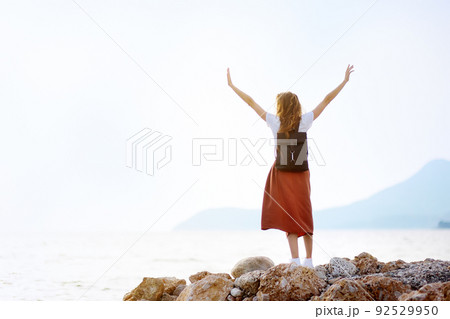 Charming young tourist woman on the Mediterranean coast. Attractive red-haired girl hiking by the sea shore. 92529950