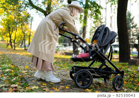 Mother with baby pram walking in autumn park Mother with baby pram walking in autumn park 92530043