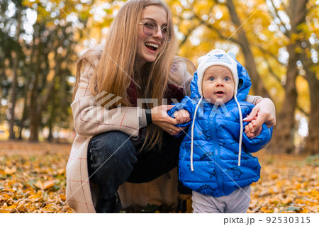 Mom teaches the kid to walk. .Young mother walks in the park with baby Mom teaches the kid to walk. .Young mother walks in the park with baby 92530315