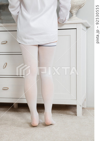 White hosiery. Beautiful long female legs in stockings. Girl putting on stockings at home in a white room. Varicose veins prevention. Woman body in underwear. White hosiery. Beautiful long female legs in stockings. Girl putting on stockings at home in a white room. Varicose veins prevention. Woman body in underwear. 92530555