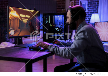 Modern player having fun with video games play competition, using computer to stream online championship. Male gamer playing rpg action tournament game at desk with neon lights. 92536386