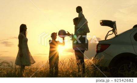 children with father mother play ball near car sunset. happy family silhouette. chidhood dream. group people picnic park. peaceful joyful man with boy son girl daughter woman wife. teamwork traveling. 92542682