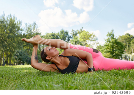 European girl in a light tracksuit doing yoga in the park in the afternoon in the summer. Gymnastics in nature. Thin woman outdoor European girl in a light tracksuit doing yoga in the park in the afternoon in the summer. Gymnastics in nature. Thin woman outdoor 92542699