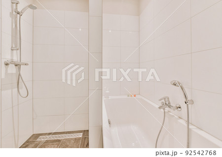 Bathtub located near shower box with glass door in modern bathroom with white tiled walls Bathtub located near shower box with glass door in modern bathroom with white tiled walls 92542768