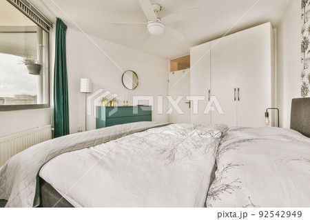 Home interior design of bedroom with bed and wooden wardrobe placed in corner near window in modern apartment 92542949