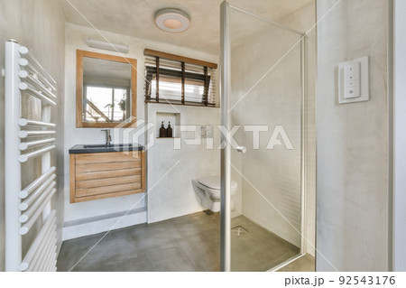 Modern flush toilet and ceramic sink installed on white tiled walls near mirror,shower box and towel in small restroom at home Modern flush toilet and ceramic sink installed on white tiled walls near mirror,shower box and towel in small restroom at home 92543176