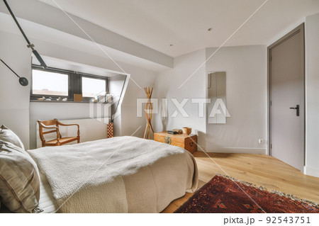 Home interior design of bedroom with bed and wooden wardrobe placed in corner near window in modern apartment Home interior design of bedroom with bed and wooden wardrobe placed in corner near window in modern apartment 92543751