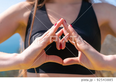 Woman makes heart with hands on beach. Young woman with long hair, fitness instructor, stretching before pilates, on a yoga mat near the sea on a sunny day, female fitness yoga routine concept 92543885