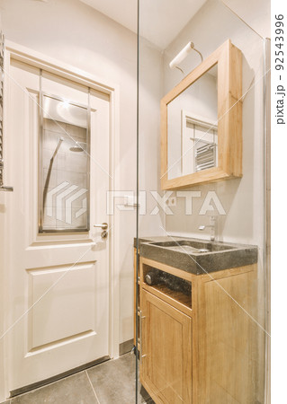 Cupboard with sink and mirror attached to tiled wall near door and drying rack in modern restroom 92543996