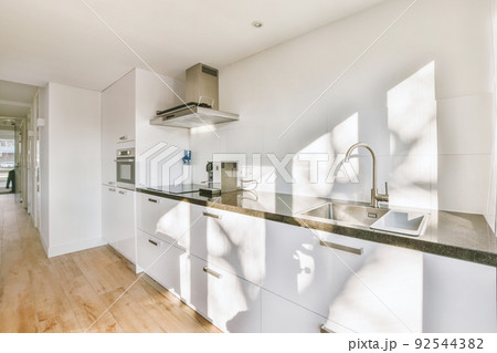 Interior of spacious light kitchen with modern white furniture and pop art portrait in light apartment 92544382