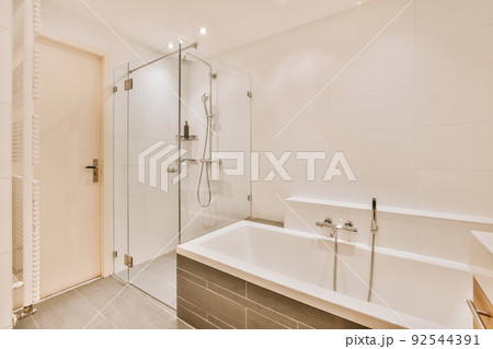 Sinks with mirrors and clean bathtub located near shower box with glass door in modern bathroom with white tiled walls 92544391