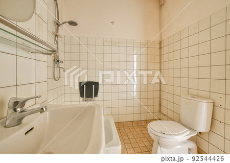 Interior of contemporary bathroom with shabby beige walls and partitions and white door at home Interior of contemporary bathroom with shabby beige walls and partitions and white door at home 92544426