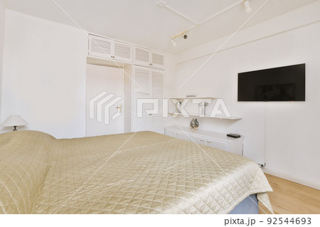 Home interior design of bedroom with bed,tv and wooden wardrobe placed in corner near window in modern apartment 92544693