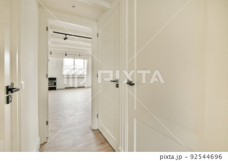Light narrow hallway with many doors in white walls and glowing lamp over lumber floor 92544696