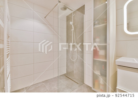 Shower faucets attached to tiled wall near glass partition and ornamental curtail in washroom at home Shower faucets attached to tiled wall near glass partition and ornamental curtail in washroom at home 92544715