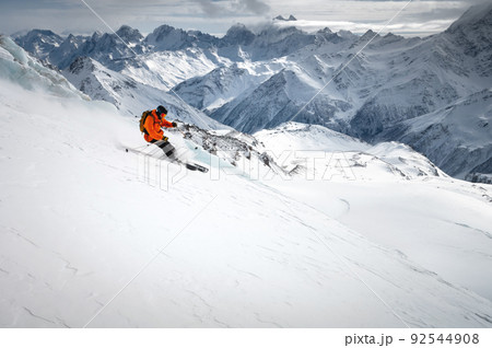 Off-piste skier on a glacier going down a beautiful alpine landscape. Blue cloudy sky in the background and high mountains. Free space for text Off-piste skier on a glacier going down a beautiful alpine landscape. Blue cloudy sky in the background and high mountains. Free space for text 92544908