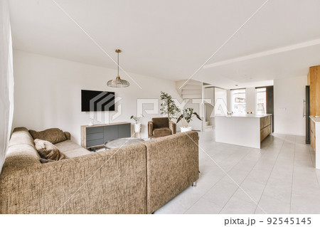 Contemporary open plan kitchen with dining table set and gray sofa in light spacious room 92545145