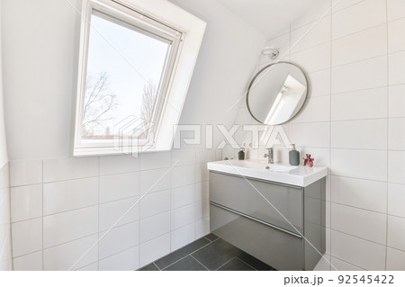 A sink with a faucet and liquid soap hangs on a tiled wall under a mirror with cosmetic products A sink with a faucet and liquid soap hangs on a tiled wall under a mirror with cosmetic products 92545422