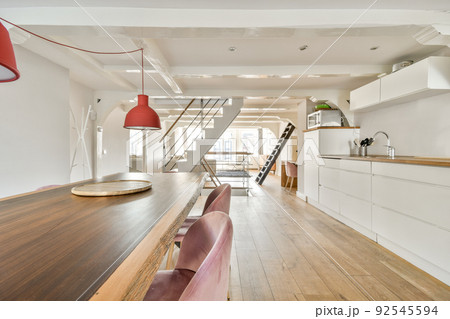 Contemporary cupboards with appliances and tables with kitchenware located in light kitchen near dining room in stylish apartment 92545594