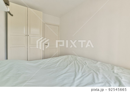 Home interior design of bedroom with bed and wooden wardrobe placed in corner near window in modern apartment 92545665
