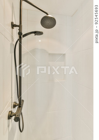 Shower faucets attached to tiled wall near glass partition and ornamental curtail in washroom at home 92545693