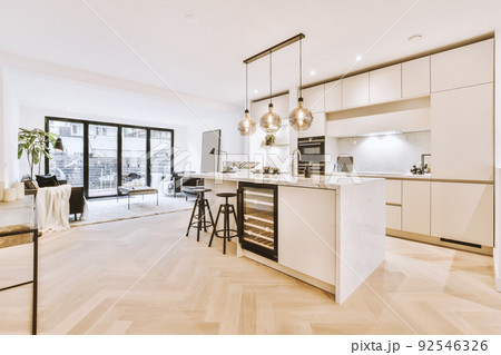White cabinets with wooden counter of modern kitchen and dining table set in living room of apartment 92546326