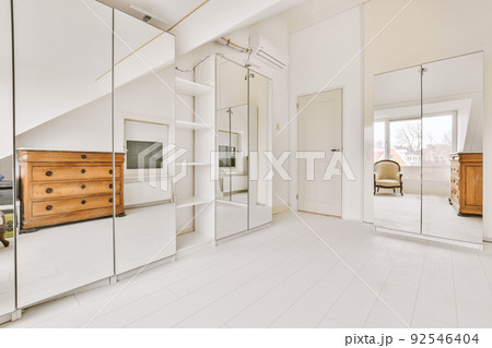 Modern cupboard and vintage chest placed near doors and wicker basket in spacious room with white walls and wooden floor 92546404