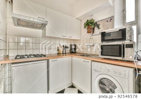 Fragment of interior of light narrow home kitchen with minimalist style white furniture with sink and stove Fragment of interior of light narrow home kitchen with minimalist style white furniture with sink and stove 92546578