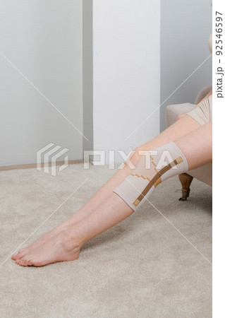 Knee support brace on a woman leg. girl in an orthosis in the interior of the house. Orthopedic anatomic braces for knee fixation, injuries and pain. Knee Joint Bandage Sleeve. Elastic Sports. Knee support brace on a woman leg. girl in an orthosis in the interior of the house. Orthopedic anatomic braces for knee fixation, injuries and pain. Knee Joint Bandage Sleeve. Elastic Sports. 92546597