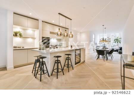 White cabinets with wooden counter of modern kitchen and dining table set in living room of apartment White cabinets with wooden counter of modern kitchen and dining table set in living room of apartment 92546622