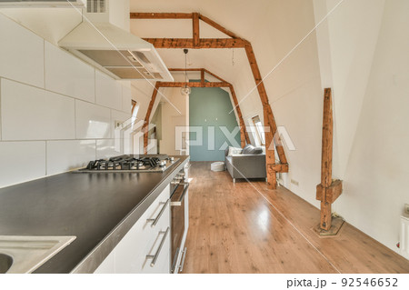 Spacious attic room of apartment with dining table and chairs near open kitchen under roof with beams 92546652