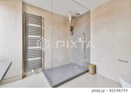 Shower faucets attached to tiled wall near glass partition and ornamental curtail in washroom at home 92546754