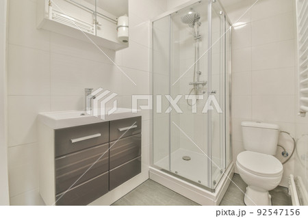 Tiled shower cabin with glass door located near sink and mirror in light restroom in contemporary apartment Tiled shower cabin with glass door located near sink and mirror in light restroom in contemporary apartment 92547156