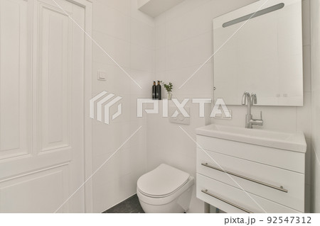 Modern flush toilet and ceramic sink installed on white tiled walls near mirror and towel in small restroom at home Modern flush toilet and ceramic sink installed on white tiled walls near mirror and towel in small restroom at home 92547312