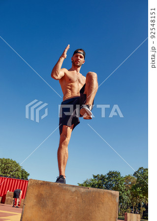 Sporty physically fit man doing step-up exercise on wooden box while doing gym training outdoor. Sporty physically fit man doing step-up exercise on wooden box while doing gym training outdoor. 92548151