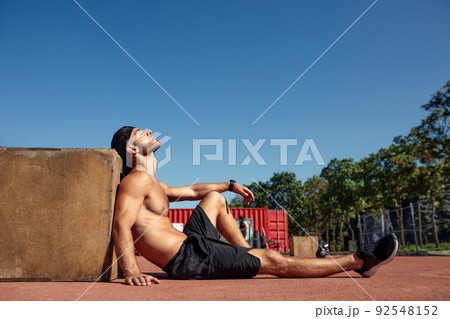 Sporty physically fit man doing step-up exercise on wooden box while doing gym training outdoor. 92548152