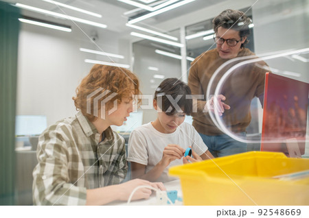 Teacher in eyeglasses explaining something to his students Teacher in eyeglasses explaining something to his students 92548669