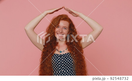 Redhead woman playing childish catching up game, feeling in safe making roof above head with hands Redhead woman playing childish catching up game, feeling in safe making roof above head with hands 92548732