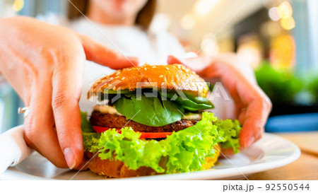 Hamburger vegan healthy vegetarian burger. Salad, avocado, vegetable on veggie sandwich eating cute woman. Tasty vegetarian healthy green food. 92550544