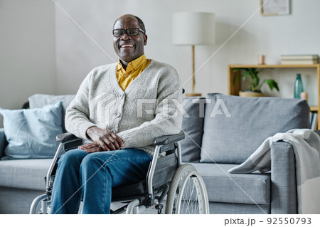 Portrait of African mature man with disability sitting in wheelchair in living room and laughing Portrait of African mature man with disability sitting in wheelchair in living room and laughing 92550793