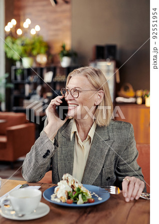 Successful mature businesswoman smiling while having conversation on mobile phone during her lunch at the restaurant 92551954