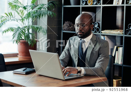 African businessman in suit sitting at the table and typing on laptop, he working online at the restaurant African businessman in suit sitting at the table and typing on laptop, he working online at the restaurant 92551968