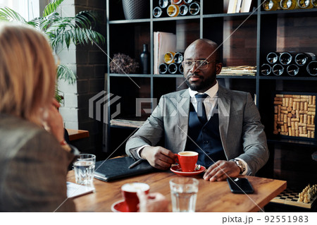 African businessman drinking coffee and talking to his colleague during coffee break at the restaurant African businessman drinking coffee and talking to his colleague during coffee break at the restaurant 92551983